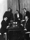 Зигберт Тарраш (справа) и Эмануил Ласкер сидят за шахматным столом. Стоят: А. Алехин, Х. Р. Капабланка, Ф. Маршалл. Санкт-Петербург. 1914